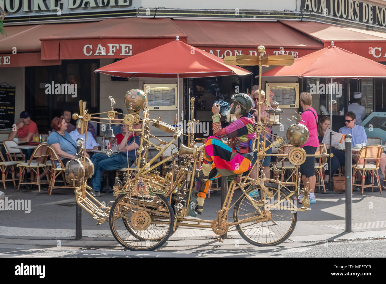 A colourfully dress eccentric looking gentleman pauses outside a Paris cafe on a futuristic looking gold tricycle. Stock Photo