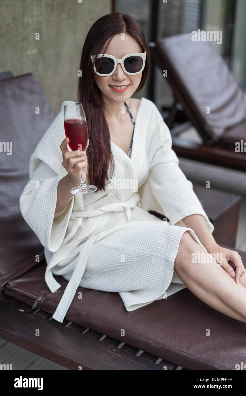woman clothed bathrobe sitting on deckchair in swimming pool Stock