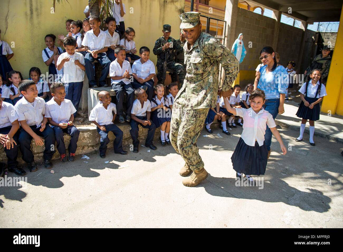 170227-N-YL073-250 TRUJILLO, Honduras (Feb. 27, 2017) – Equipment Operator 2nd Class Elijah Godbold, a native of Augusta, Ga., assigned to Construction Battalion Maintenance (CBMU) 202, plays dances with a Honduran elementary school child during a  U.S. Fleet Forces (USFF) Band performance in support of the Continuing Promise 2017's (CP-17) visit to Trujillo, Honduras. CP-17 is a U.S. Southern Command-sponsored and U.S. Naval Forces Southern Command/U.S. 4th Fleet-conducted deployment to conduct civil-military operations including humanitarian assistance, training engagements, and medical, den Stock Photo