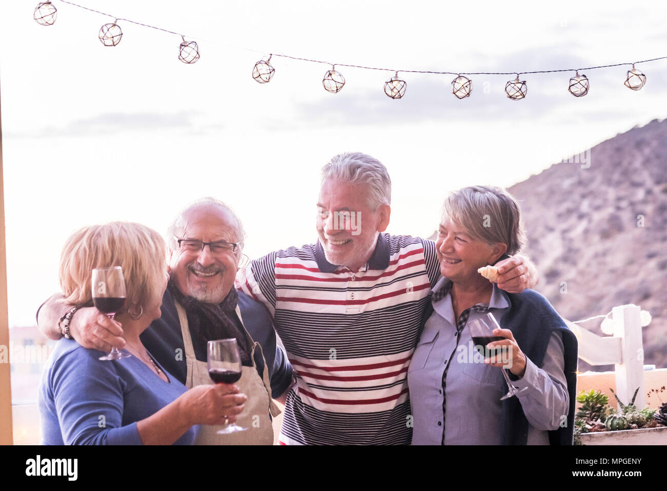 group of 4 seniors, two couples, stay togheter and have fun enjoing a cup of wine outdoor in the rooftop. vacation elderly concept and friendship. sun Stock Photo