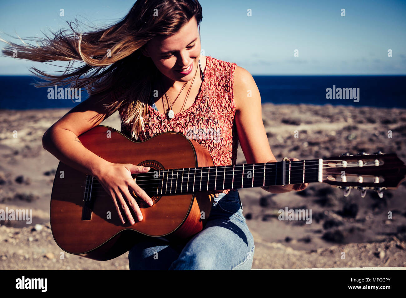 beautiful caucasian female in leisure activity outdoor with an acoustic guitar and the ocean in background. freedom rebel summer concept in tenerife Stock Photo