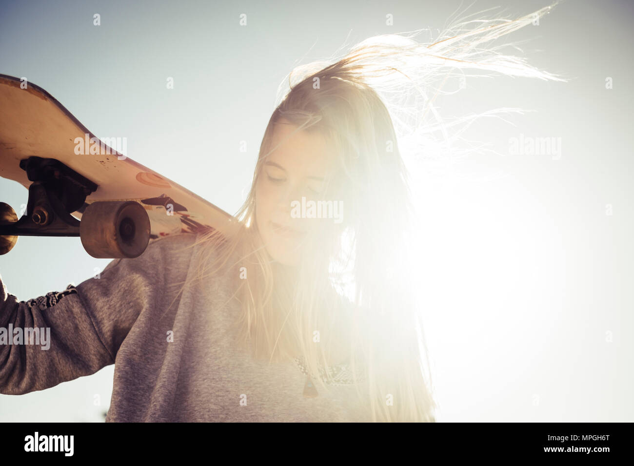 sun backlight and blonde young woman with skateboard. closed eyes