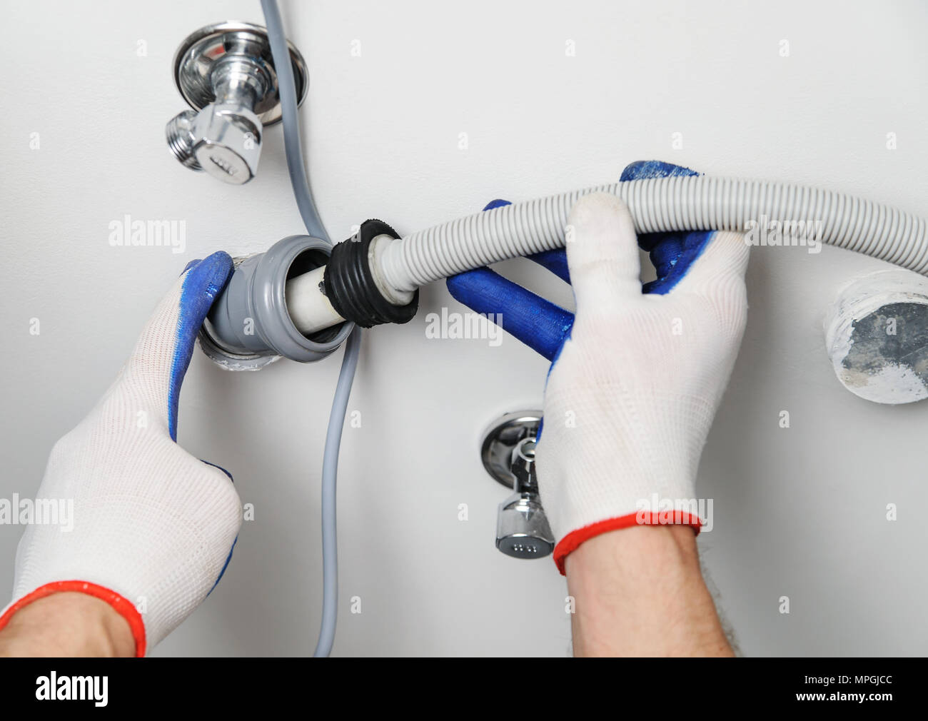 Installation of household appliances. Workman attaches a drain hose to a sewage pipe. Stock Photo