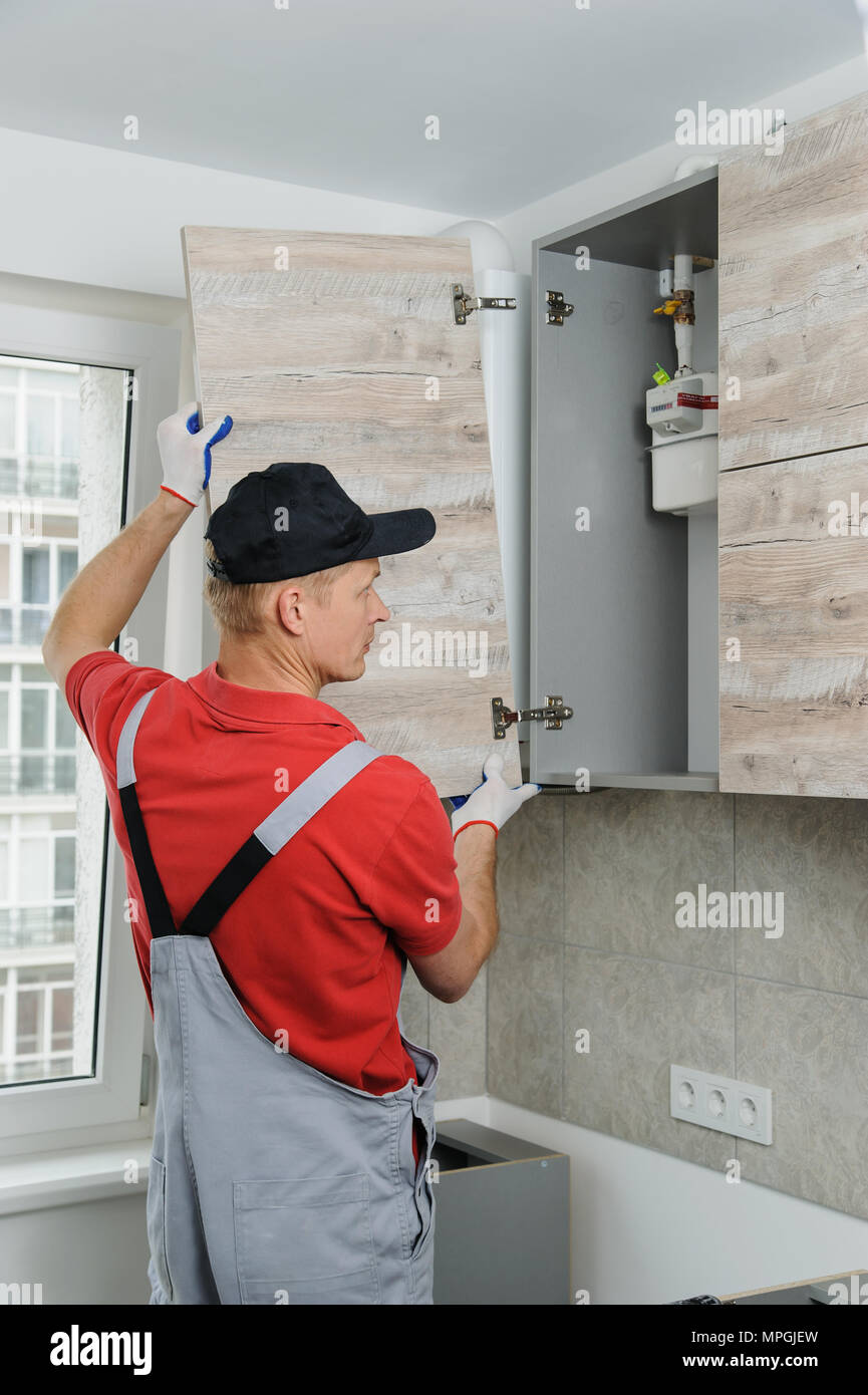 Installation of kitchen. Workman installs doors to kitchen cabinet. Stock Photo