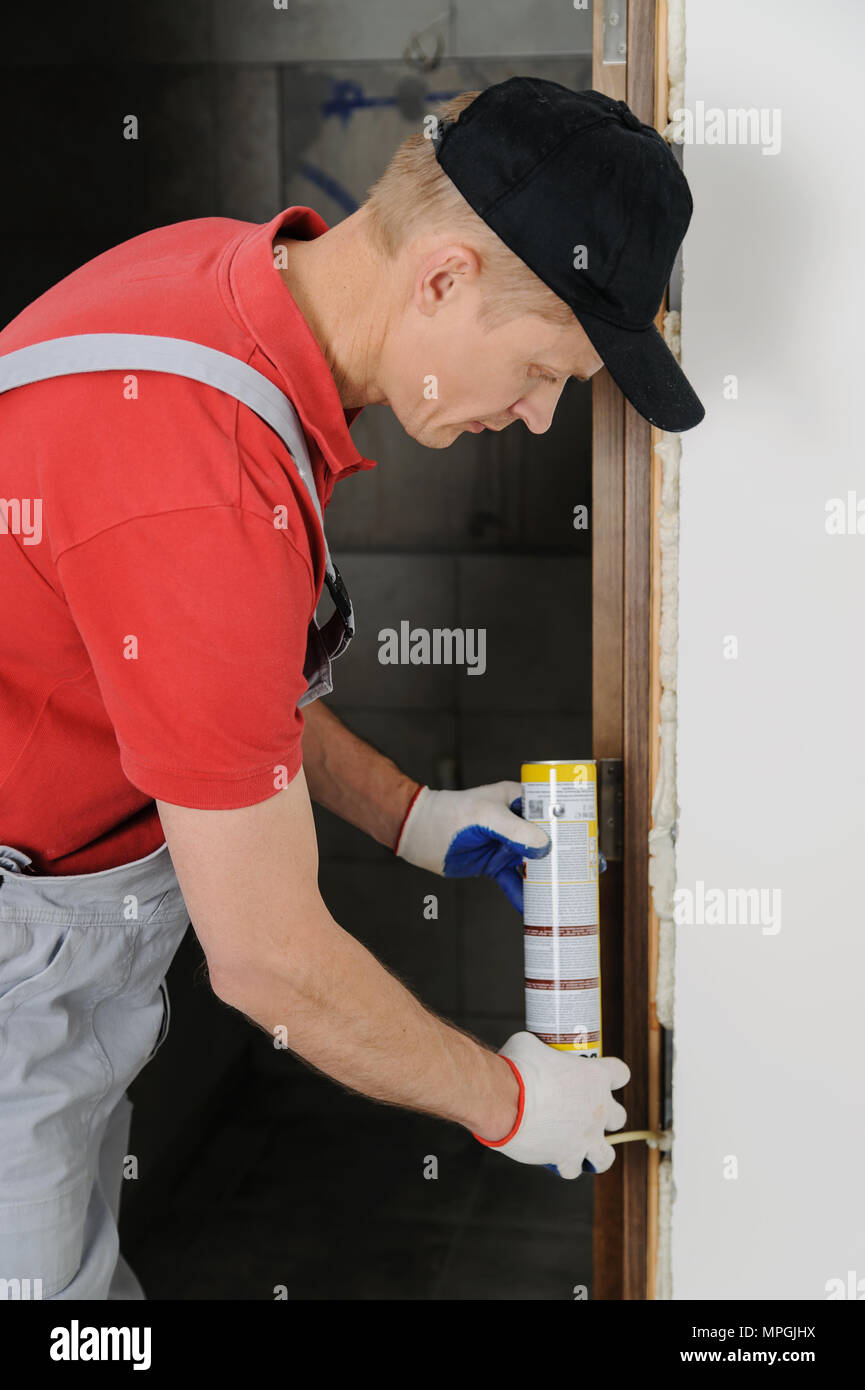 Installing door unit. Workman fixed the door frame using mounting foam. Stock Photo