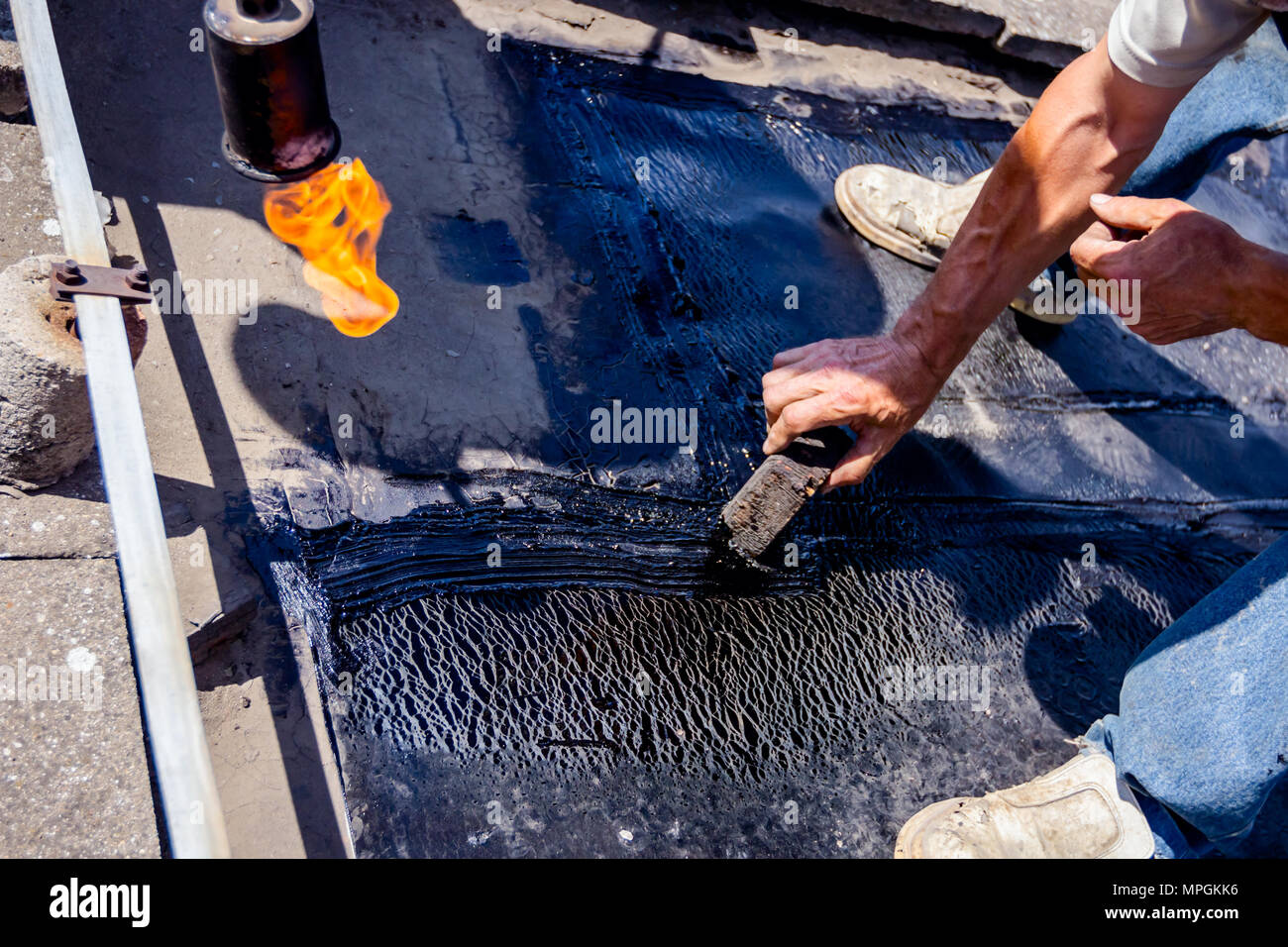 Heating and melting of bitumen surface by flame from gas torch. Worker  adjusts bituminous cover for roofing felt, smears melted resin with wooden  tool Stock Photo - Alamy