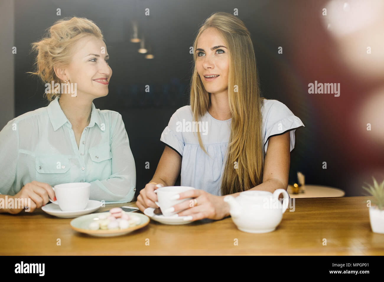 Two cheerful charming young women drinking coffee and talking in cafe Stock Photo