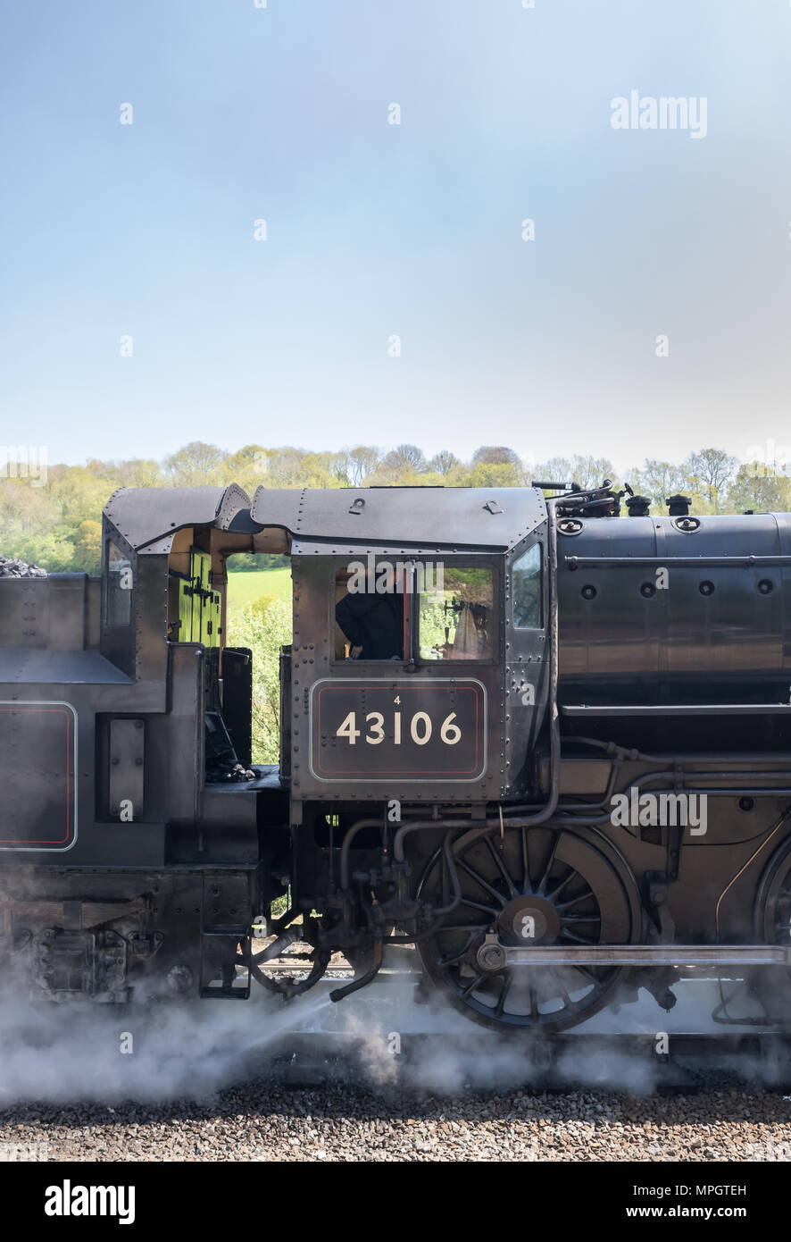Close-up, portrait side view of vintage UK steam train 43106 passing through English countryside on sunny day, train crew inside locomotive cab. Stock Photo
