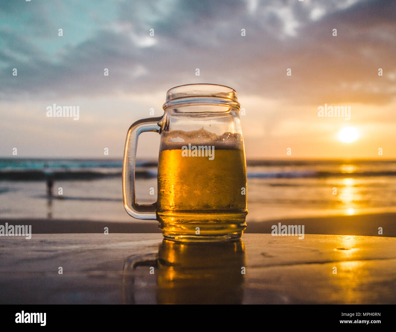 Glass jar of beer on a wooden table looking out at the ocean during