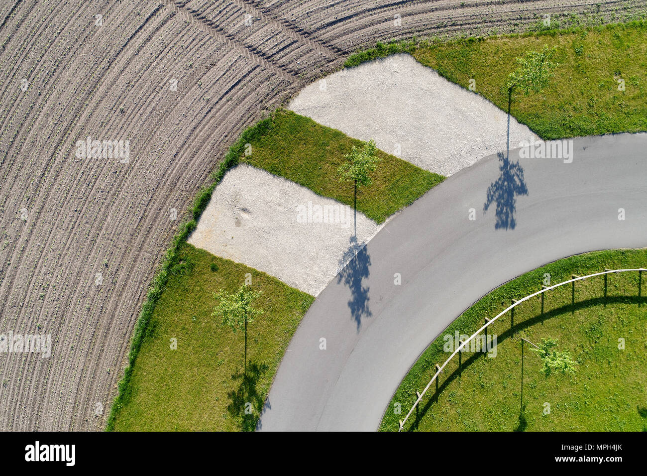 Abstract aerial view of the shadow of three trees standing at the edge of a curve on a path next to a field, made with drone Stock Photo