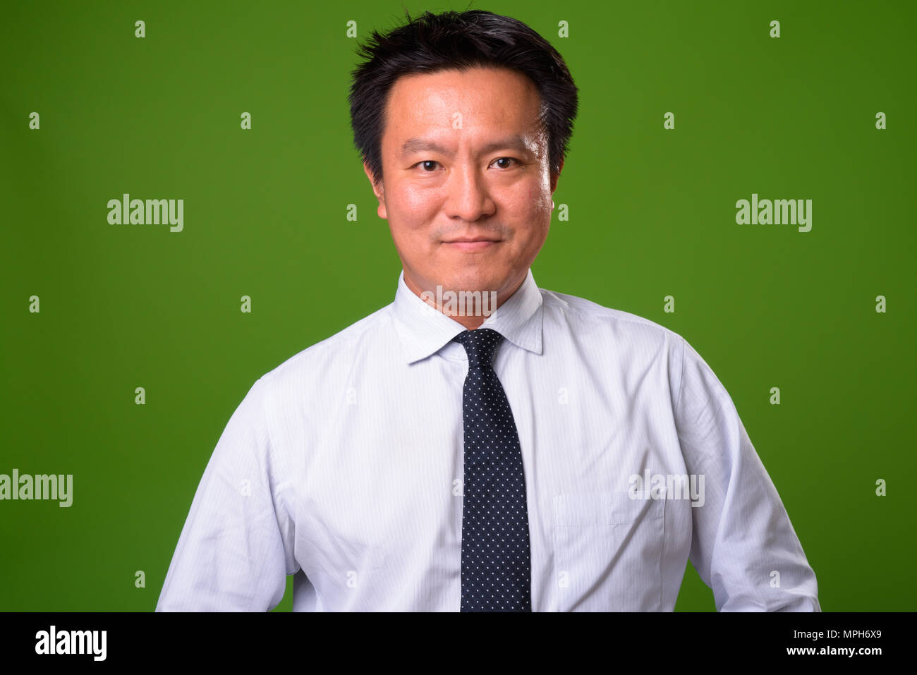 Mature Japanese businessman against green background Stock Photo
