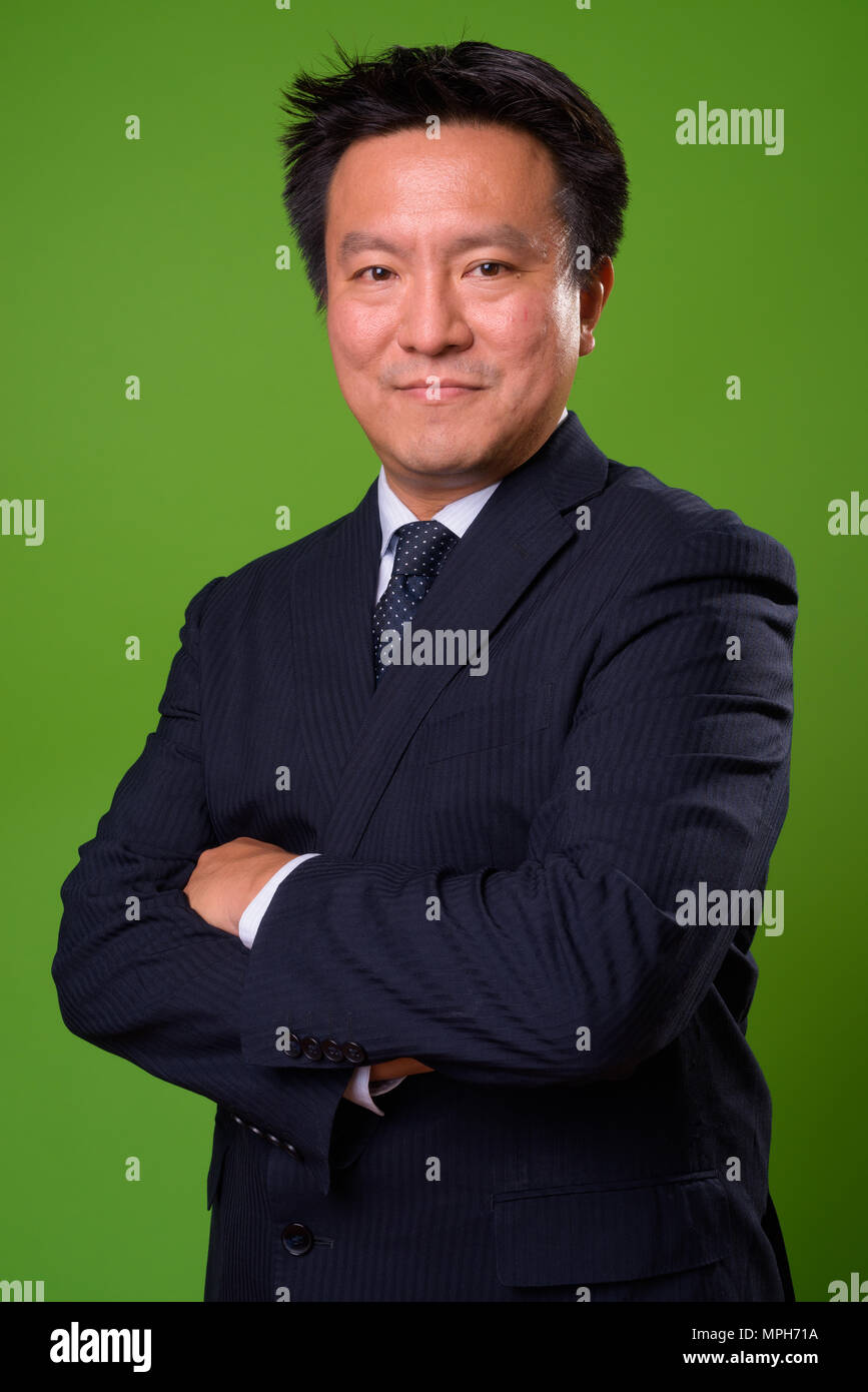 Mature Japanese businessman against green background Stock Photo