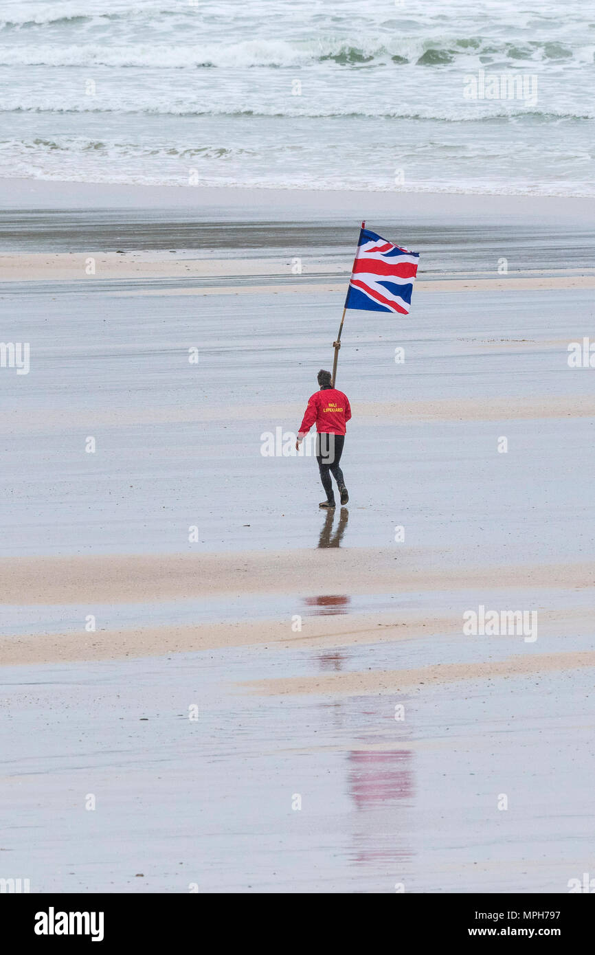A RNLI Lifeguard carrying a Union Jack Union Flag marker flag on Fistral Beach in Newquay Cornwall Stock Photo