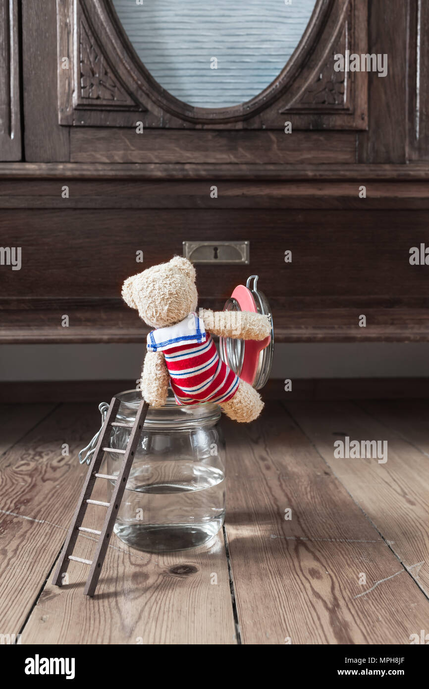 Nostalgic scene teddy bear in swimsuit with sailor collar take bath for refreshment inside room with old furniture at canning jar and ladder outside Stock Photo