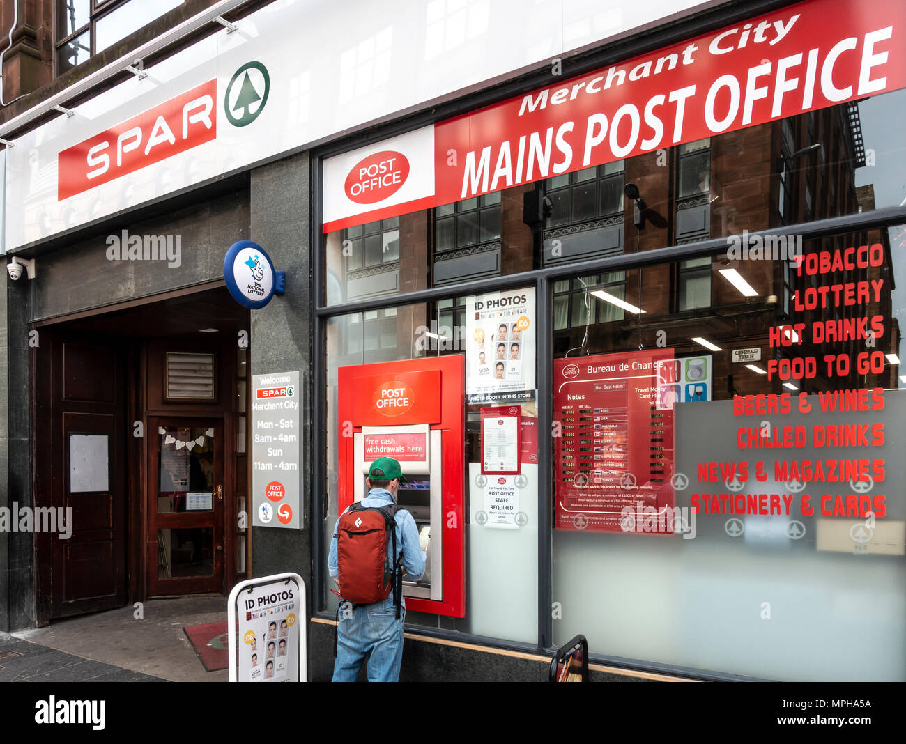 Man using a cashpoint / ATM outside the Post Office / Spar shop in Glassford St, Merchant City, Glasgow, Scotland, UK, Stock Photo