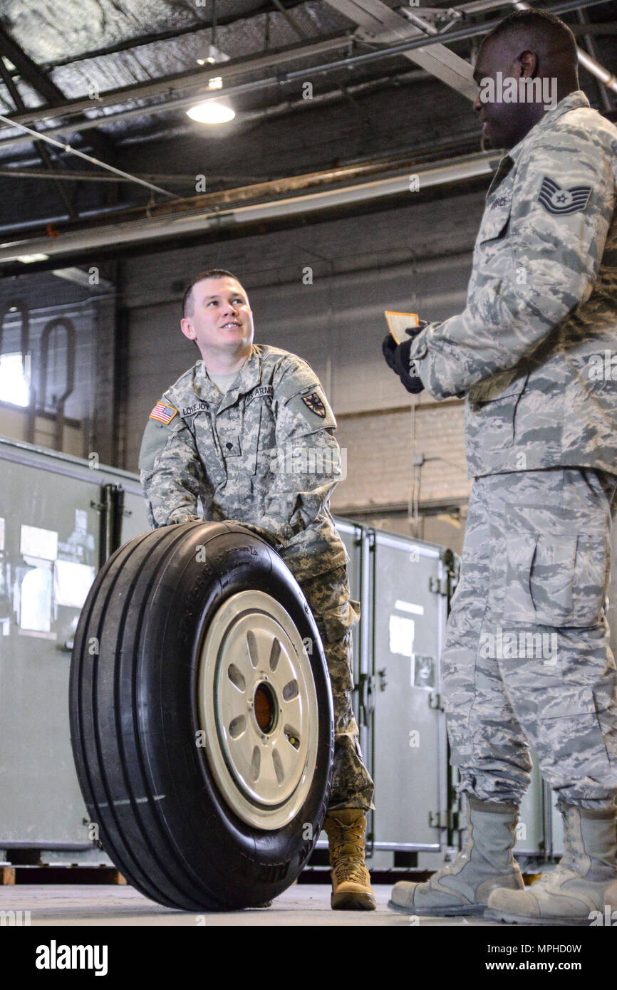 U.S. Army Spc. Eugene Lovejoy, 368th Seaport Operations Company, 11th Transportation Battalion, 7th Transportation Brigade (Expeditionary) motor pool clerk, left, receives guidance from U.S. Air Force Tech. Sgt. Jeremy Roberts, 733rd Logistic Readiness Squadron readiness spares package NCO in charge, right, on how to properly load a tire at Joint Base Langley-Eustis, Va., March 2, 2017. The 733rd LRS worked with the 7th Transportation Brigade’s supply specialists during a week-long training to showcase the Air Force’s supply management processes. (U.S. Air Force photo by 1st Lt. Mahalia Frost) Stock Photo