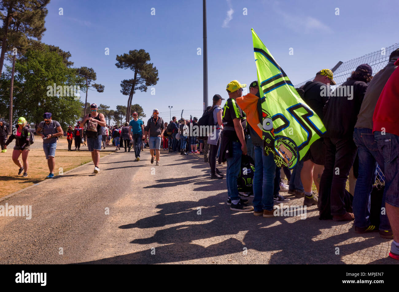 19-20th May 2018. Le Mans, France.  Behind the scenes at the MotoGP.  Spectators line the perimeter fence of the race circuit to watch the MotoGP practice session.  Meanwhile, other fans walk along the dirt road behind in search of refreshments or alternative viewing locations.  One of the spectating fans holds a number 46 flag, demonstrating his support of Valentino Rossi. Stock Photo