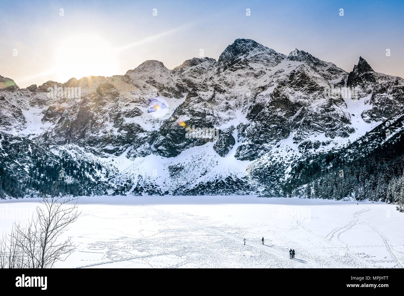 View on the rocky mountains covered with snow during sunrise and frozen lake at the bottom of the mountains. Stock Photo