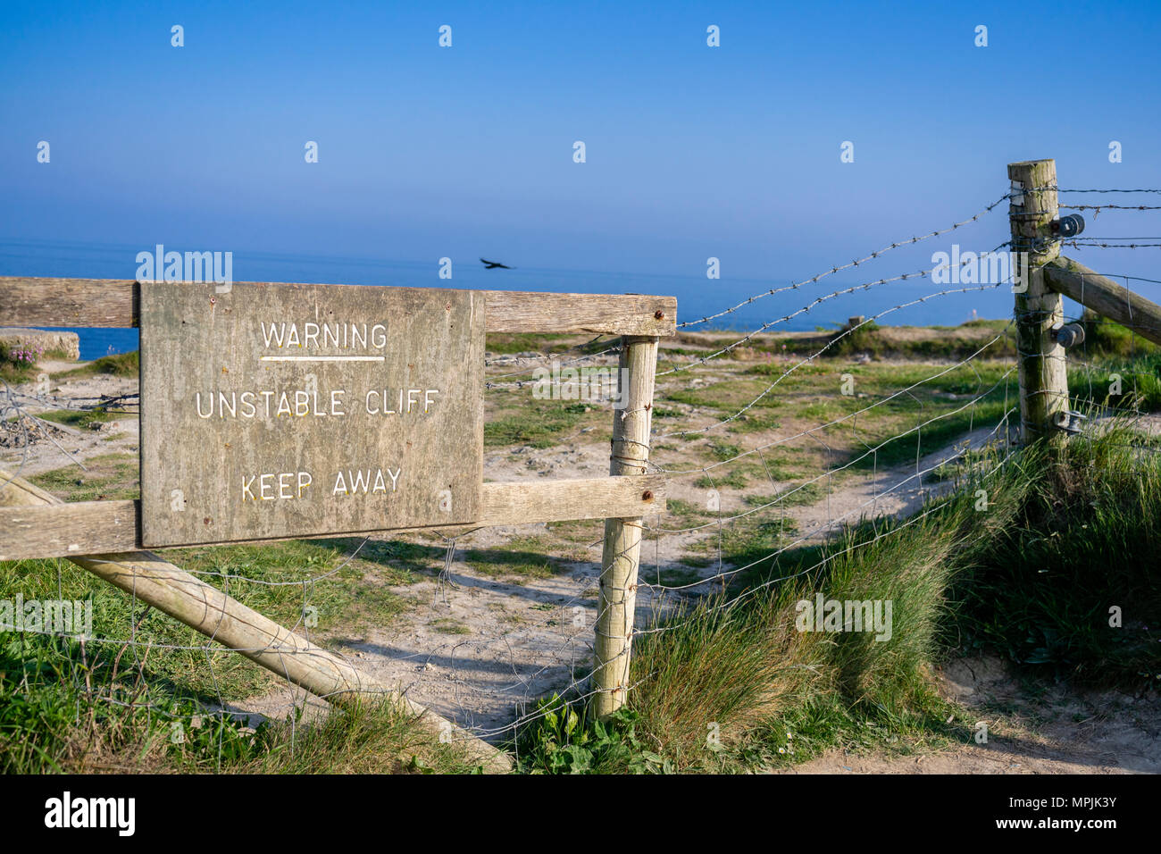 A wooden warning sign advising of an unstable cliff - keep away at the Jurassic Coast in Dorset, England, UK Stock Photo