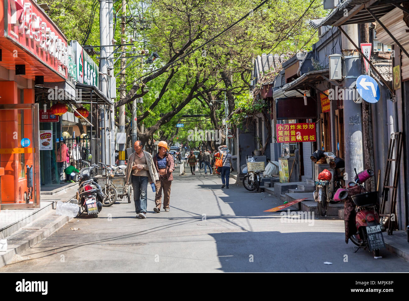 A pair of workmen stroll down a street in Beijing. One exposes his abdomen in order to cool down in the midday heat. Stock Photo