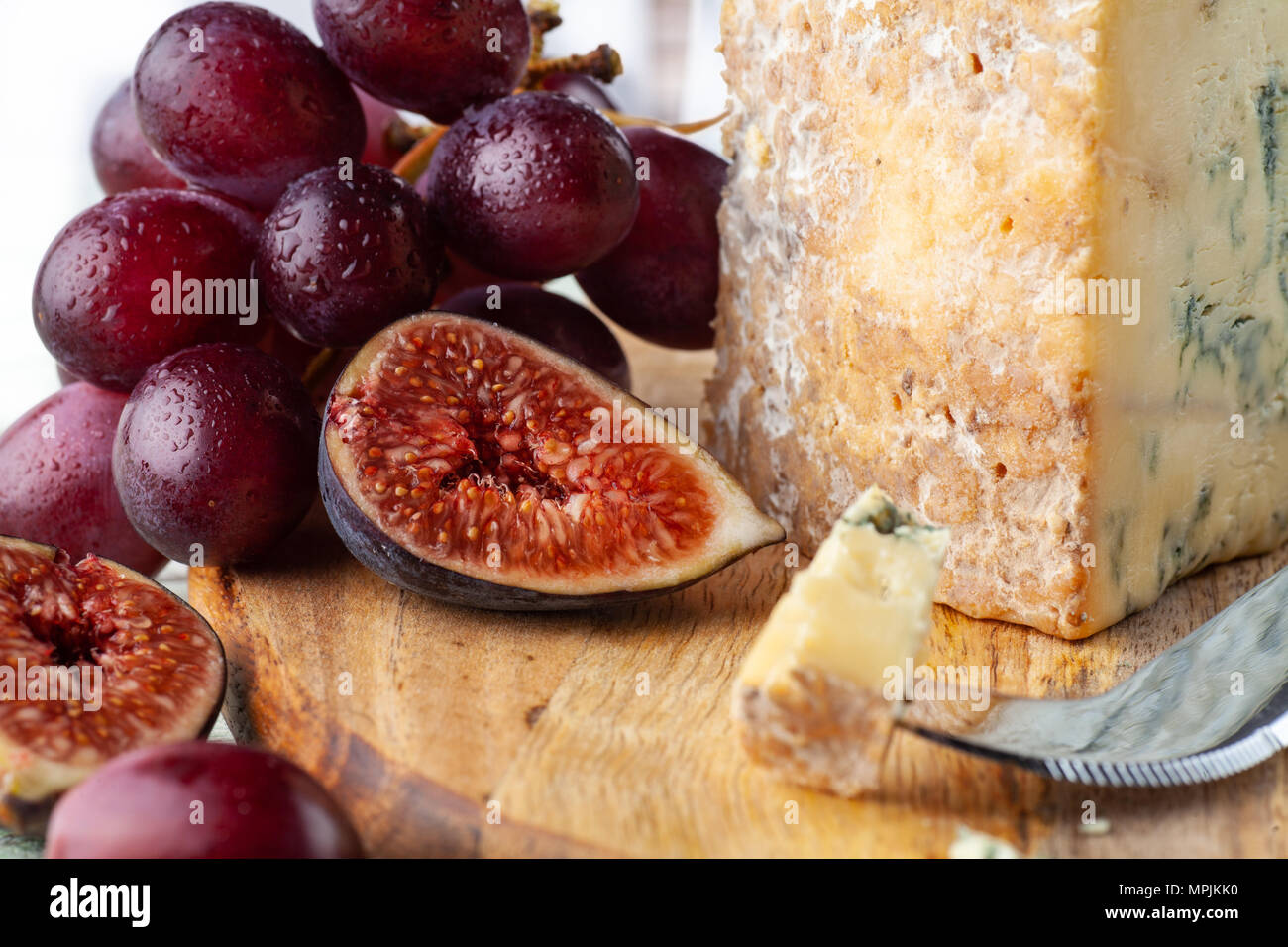 Stilton on a cheese board with red grapes, fig and cheese knife Stock Photo