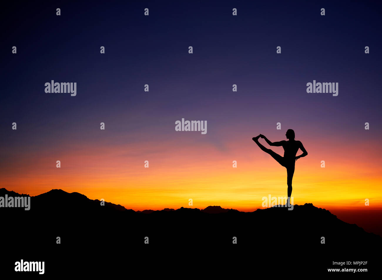 Fit Man in silhouette doing yoga balance pose at beautiful orange sunset sky background Stock Photo