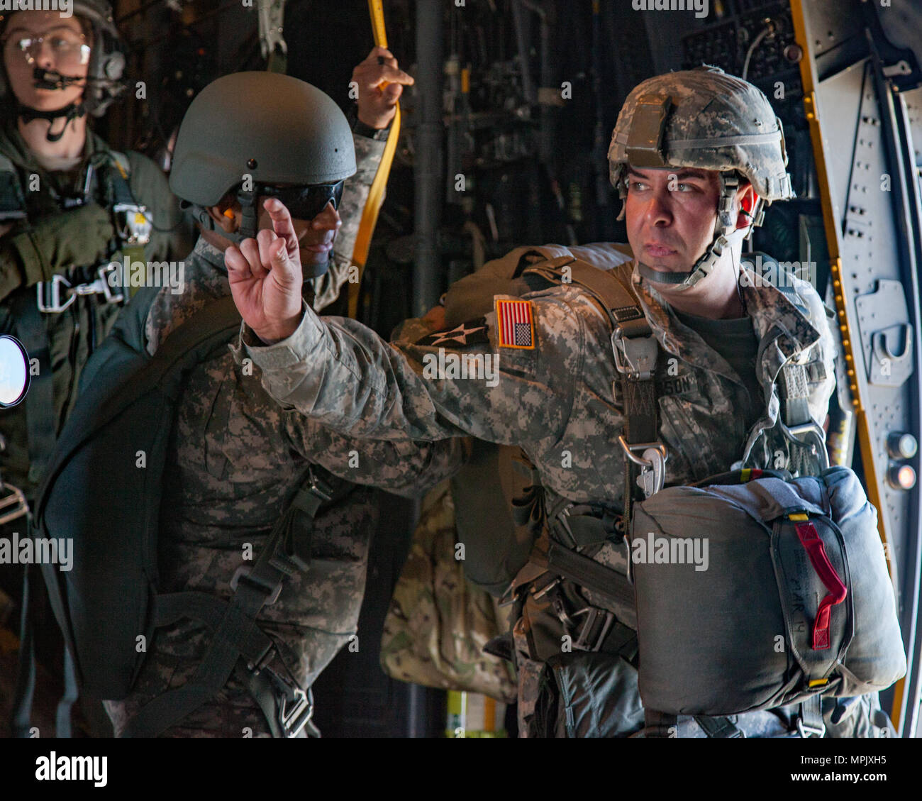 U.S. Army Sgt. 1st Class Andrew Severson of the 15th Psychological Operations Battalion uses hand signals to communicate with another JumpMaster during a static line jump over Augusta, Ga., March 3, 2017. The paratroopers jump to fulfill Airborne obligations while also building confidence and experience, ensuring they remain mission capable. (U.S. Army photo by Spc. Jesse Coggins/Released) Stock Photo
