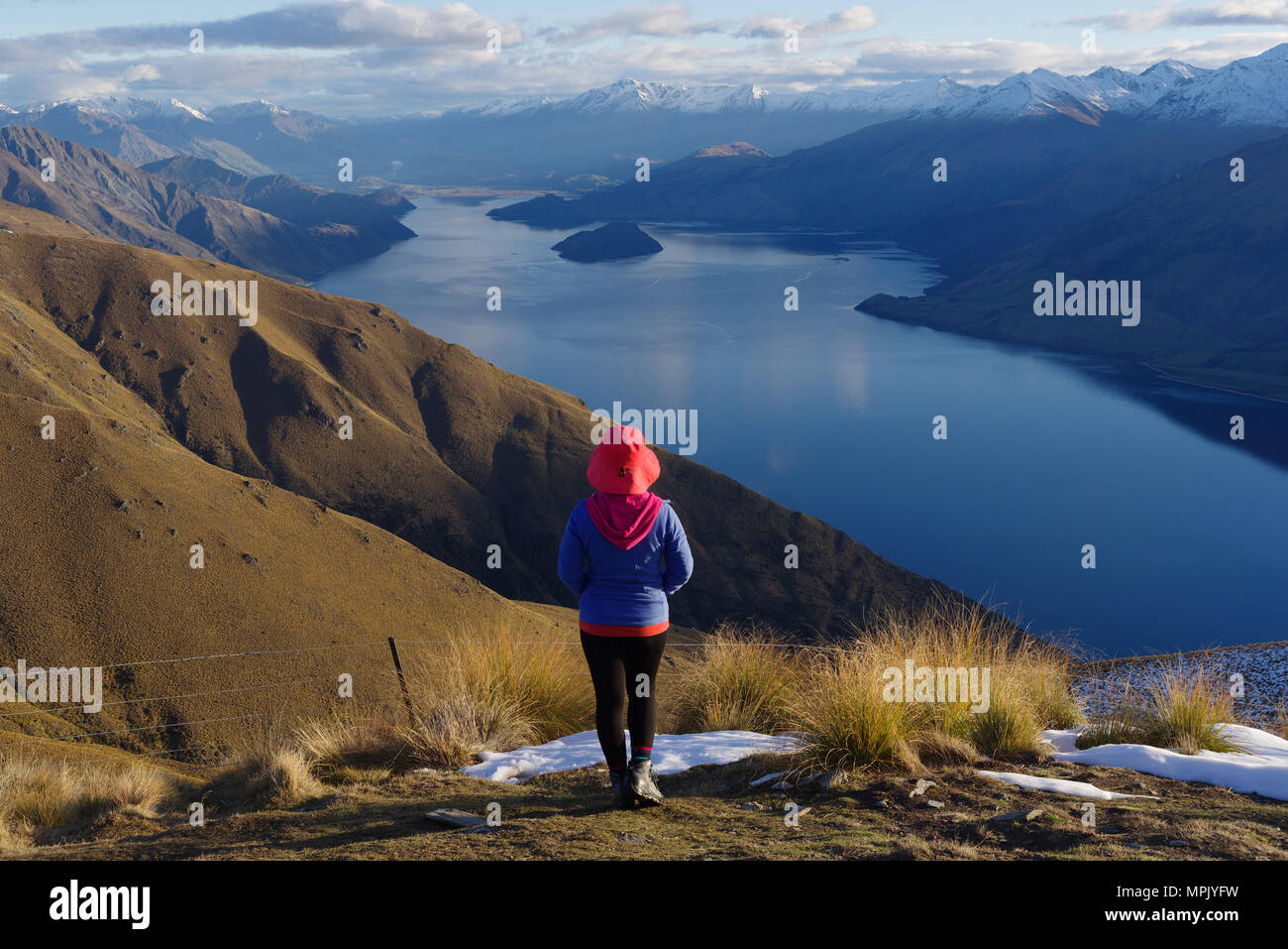 Lady hiker standing on top of the mountain - isthmus peak with a view of the Wanaka Lake in the afternoon Stock Photo