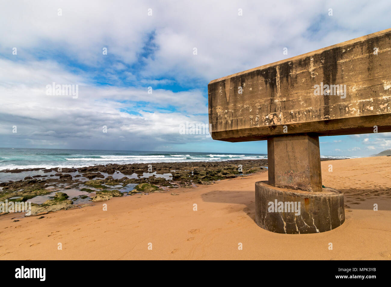 Concrete drainage pipeline extending onto sandy beach against rocky