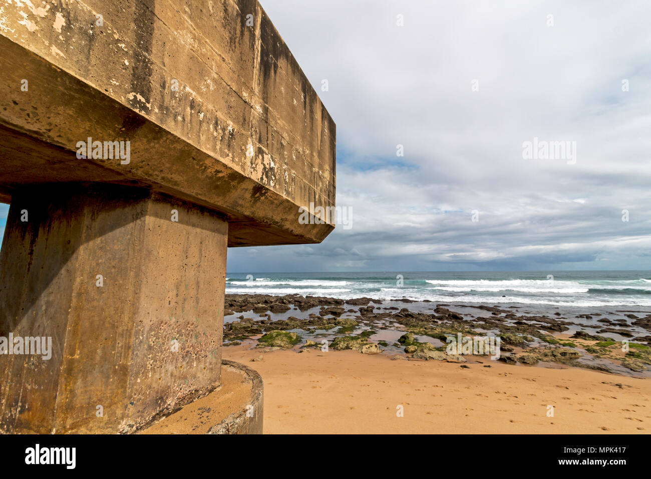 Concrete drainage pipeline extending onto sandy beach against rocky