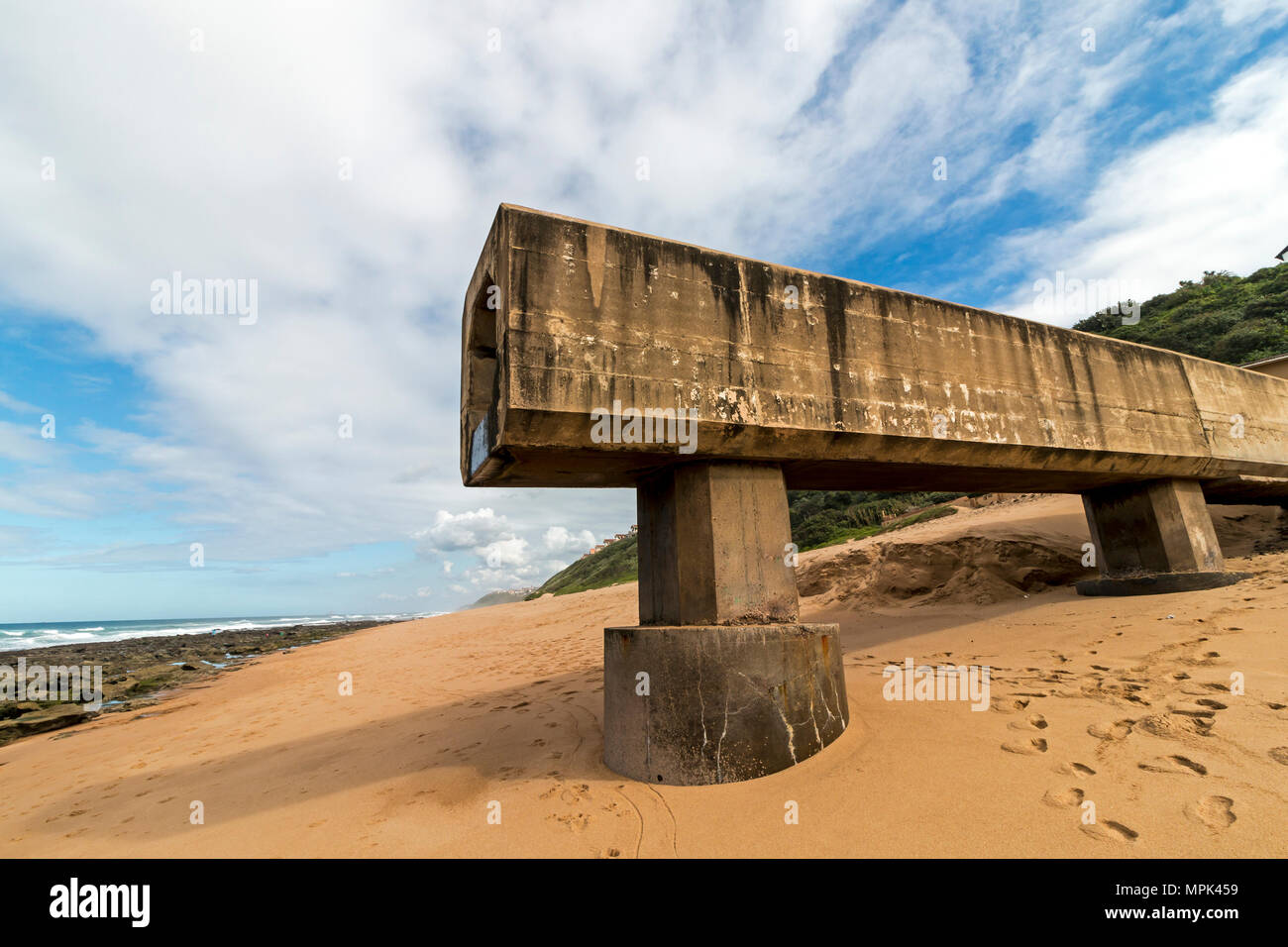 Concrete drainage pipeline extending onto sandy beach against rocky