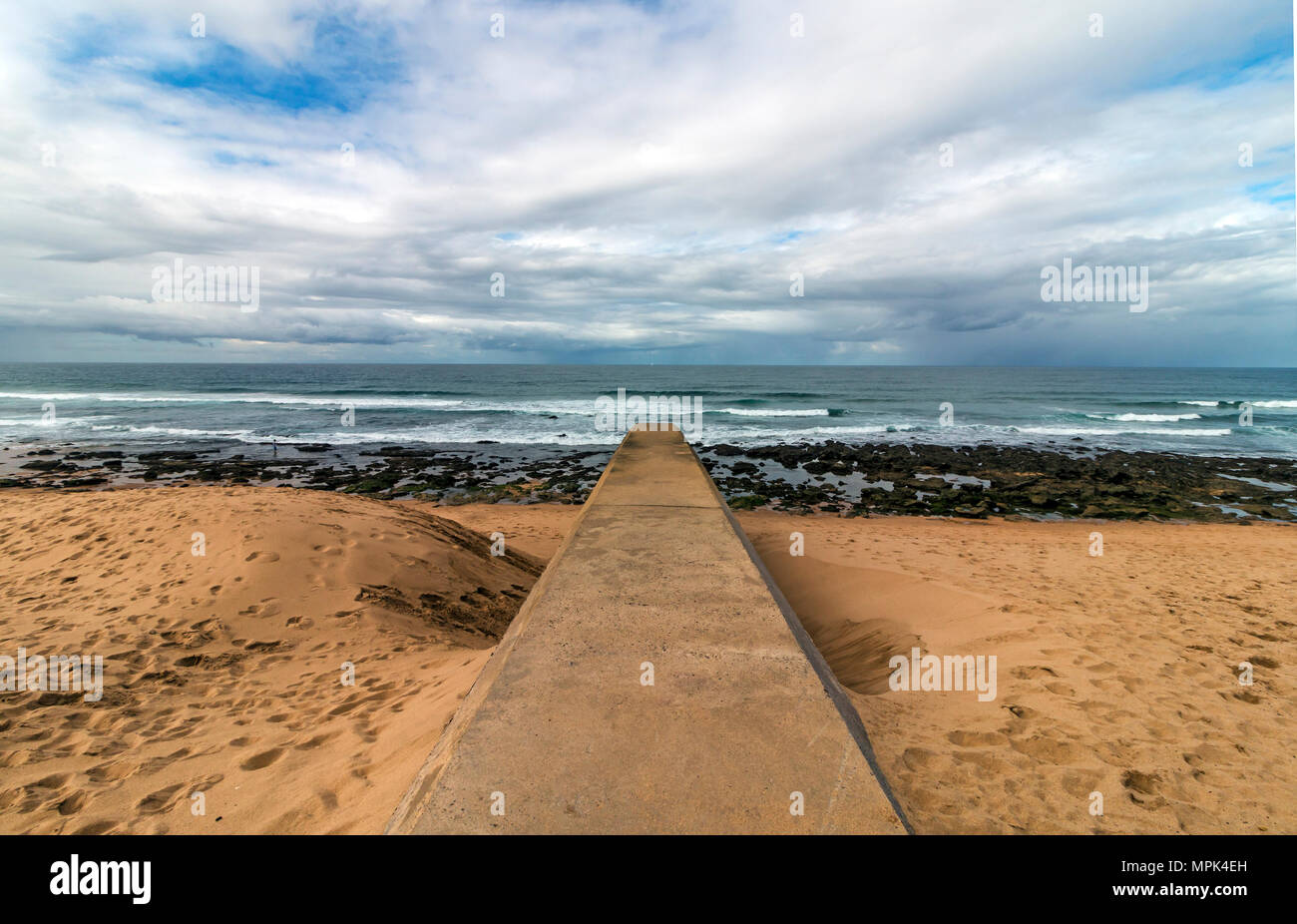 Concrete drainage pipeline extending onto sandy beach against rocky