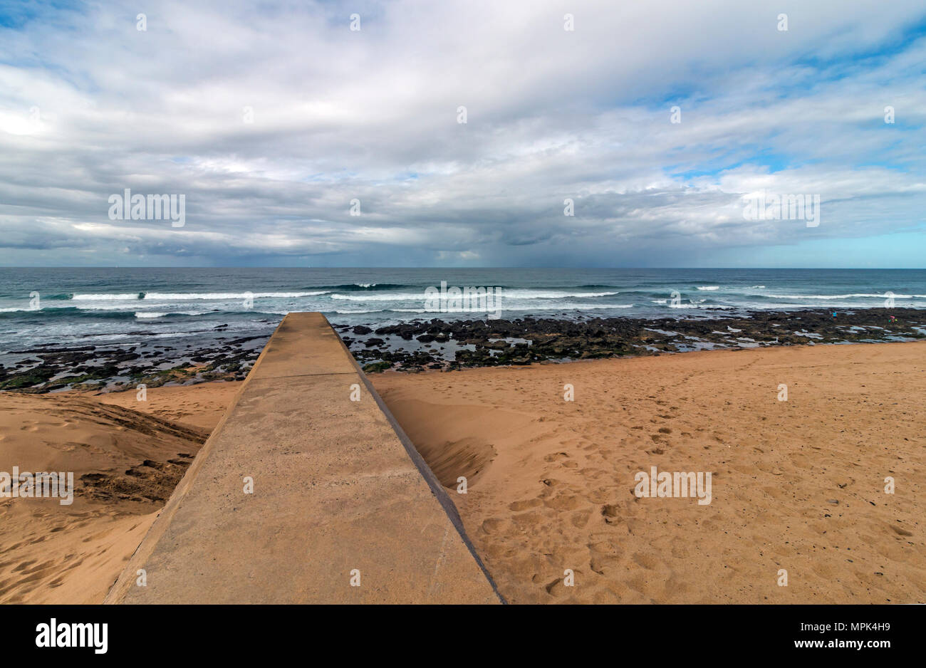 Concrete drainage pipeline extending onto sandy beach against rocky