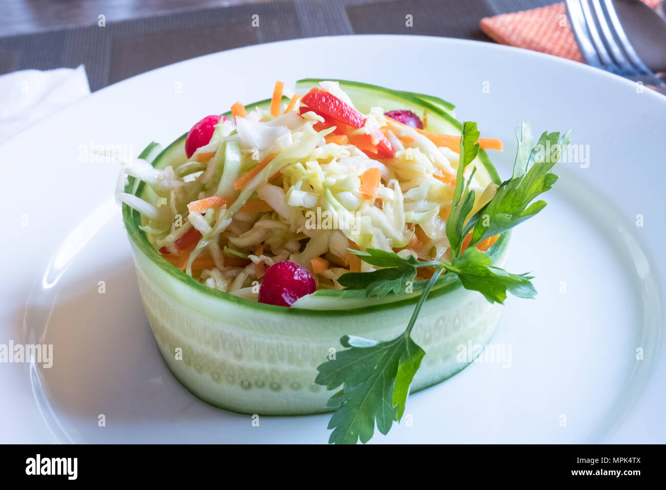 Salad from raw cabbage, carrot, pepper, cucumber and cranberries on a white plate Stock Photo