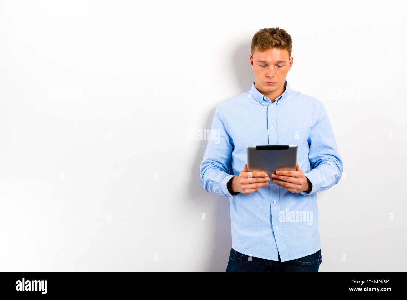 Young man using tablet and standing against white wall. Stock Photo