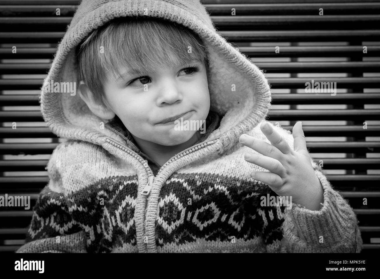 18 month old boy in hooded cardigan sat on bench in black and white Stock Photo