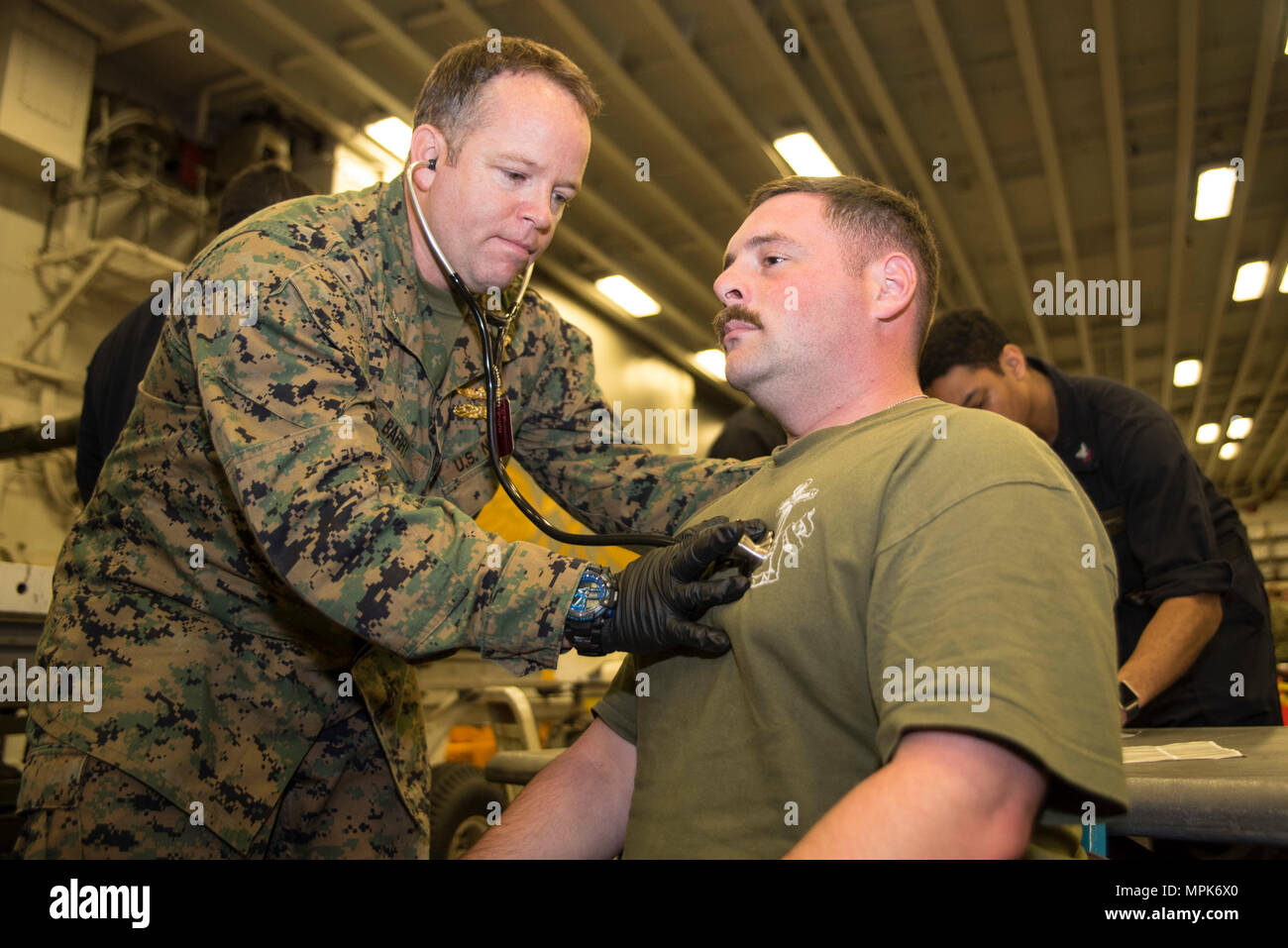170323-N-XT039-235 PHILIPPINE SEA (March 23, 2017) Cmdr. Michael Barry, left, from Clarksville, Tenn., assigned to Combat Logistics Battalion (CLB) 31 of the 31st Marine Expeditionary Unit (MEU), conducts a medical screening exam on Hospital Corpsman 3rd Class Jared Kepler, from Maple Valley, Wash., during a simulated non-combatant evacuation operation (NEO) in the hangar bay of the amphibious assault ship USS Bonhomme Richard (LHD 6) as part of a certification exercise (CERTEX). A NEO is an exercise conducted to ensure commands can quickly and efficiently complete the task of evacuating non-c Stock Photo