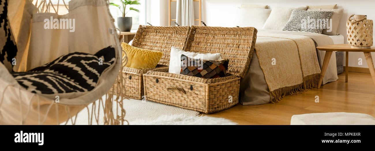 Decorative pillows placed in two straw baskets standing next to a bed