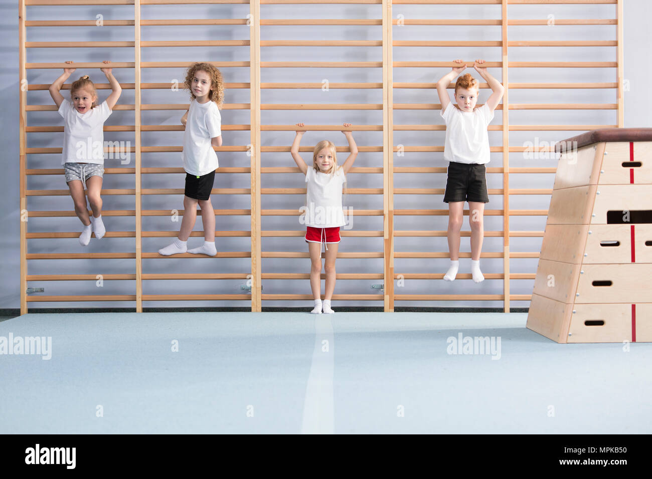 Young, active school boys and girls standing and hanging from wall bars, warming up for physical education athletics class Stock Photo