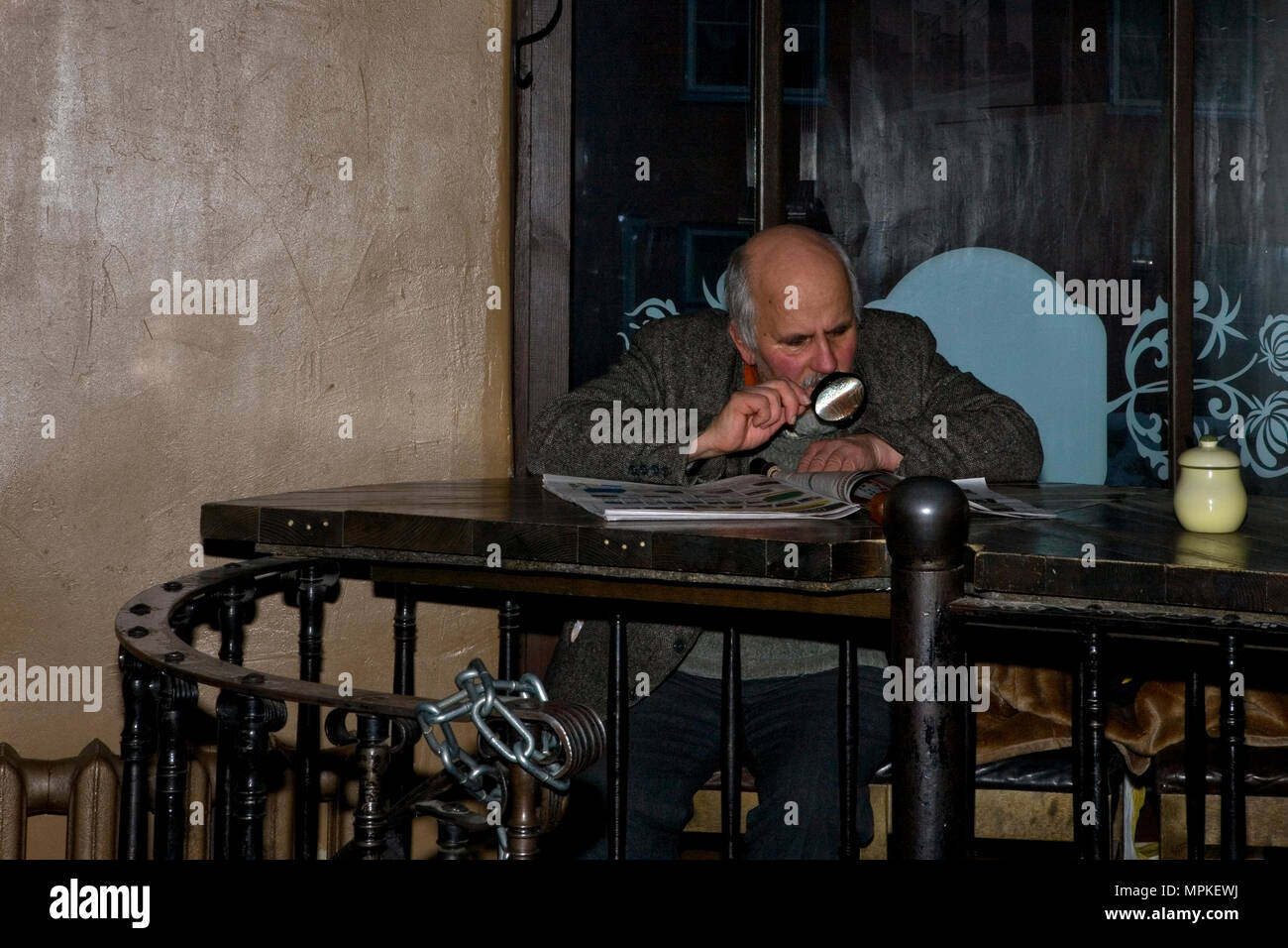 Interior, Hell Hunt (The Gentle Wolf), Pikk 39, Tallinn, Estonia: old man reads the paper with the help of a magnifying glass Stock Photo