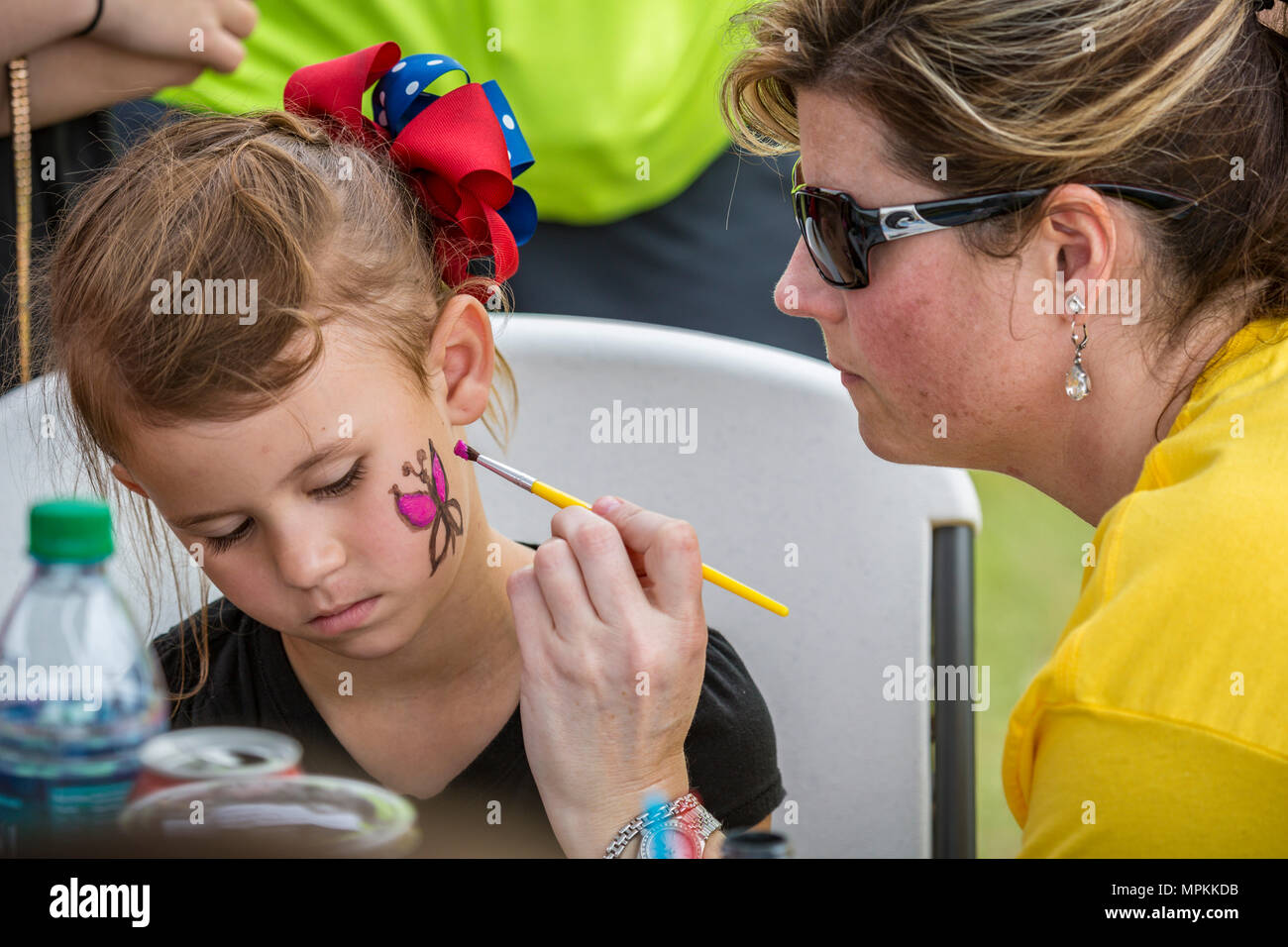 Woman painting a pink butterfly on the cheek of a young girl during a Springfest fundraiser at Crosspoint Church in Gulfport, Mississippi Stock Photo