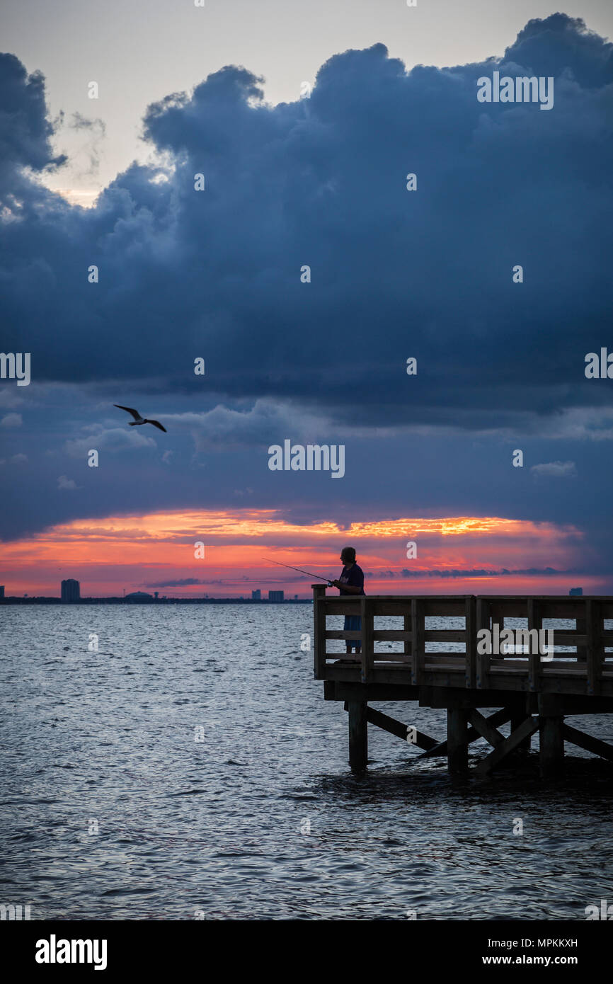 Fisherman on fishing pier under dramatic cloudy sunrise in Gulfport, Mississippi, USA Stock Photo