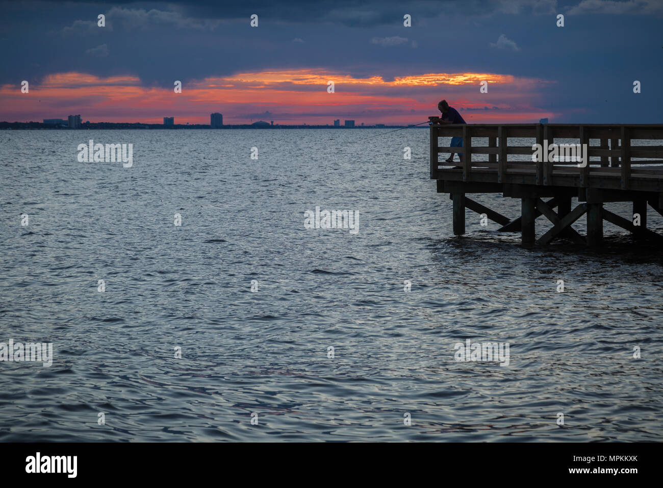 Fisherman on fishing pier under dramatic cloudy sunrise in Gulfport, Mississippi, USA Stock Photo