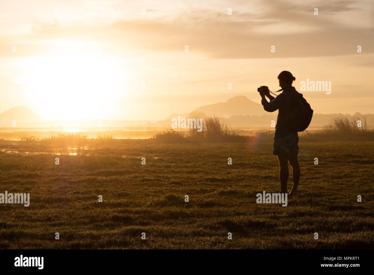 silhouette of a woman holding a smartphone taking pictures outside during sunrise or sunset. Stock Photo
