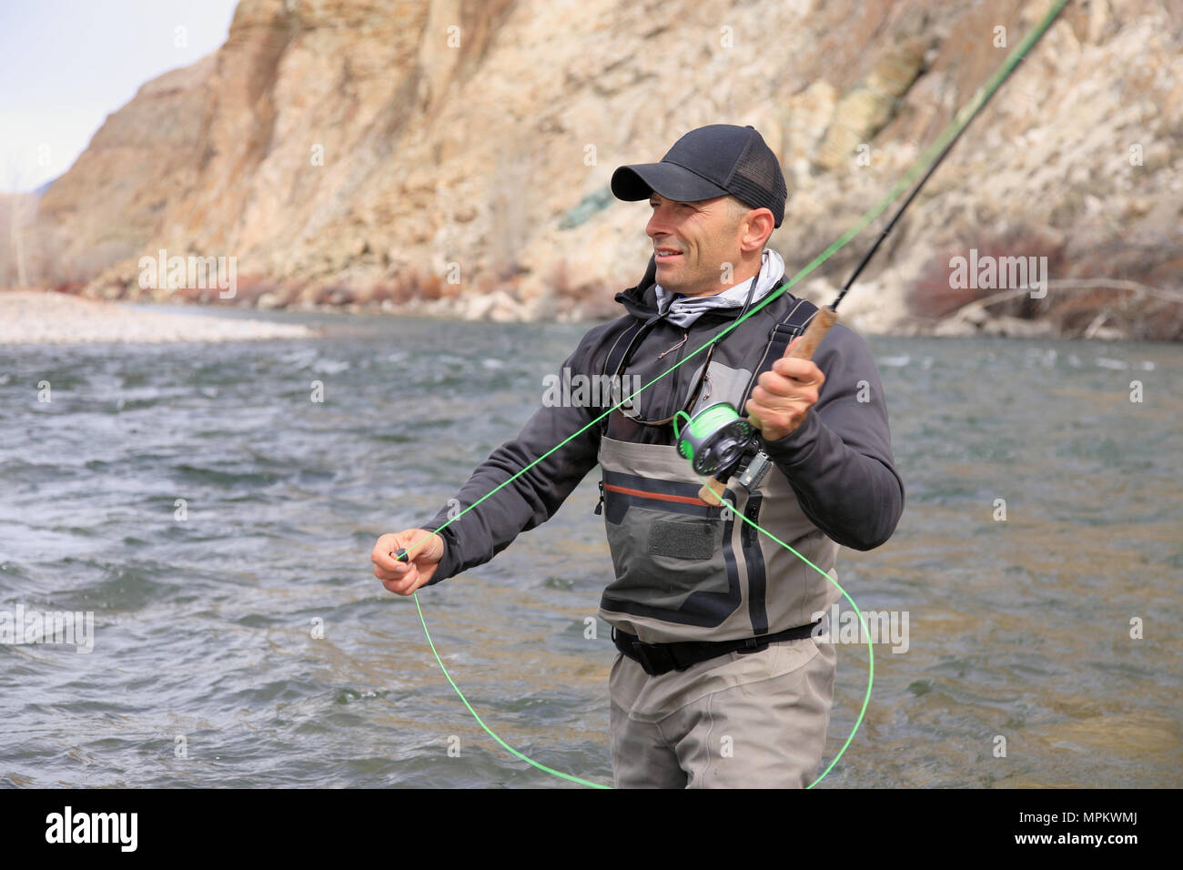 adult male fisherman wading and casting a fly rod on a river Stock Photo