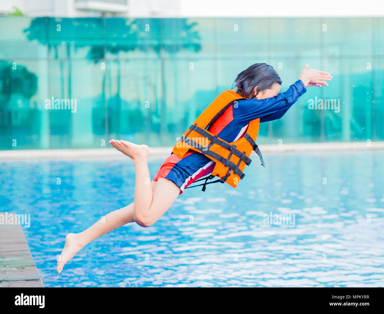 Happy little boy wearing orange life jacket has fun and enjoy jumping in the swimming pool. Focus on boy body. Stock Photo