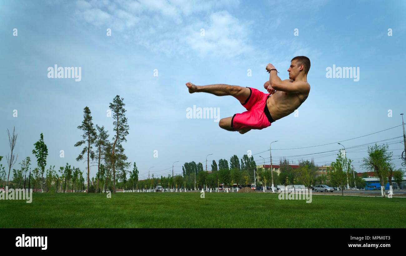 Tricking on lawn in park. Man makes kick in jump with turn. Martial