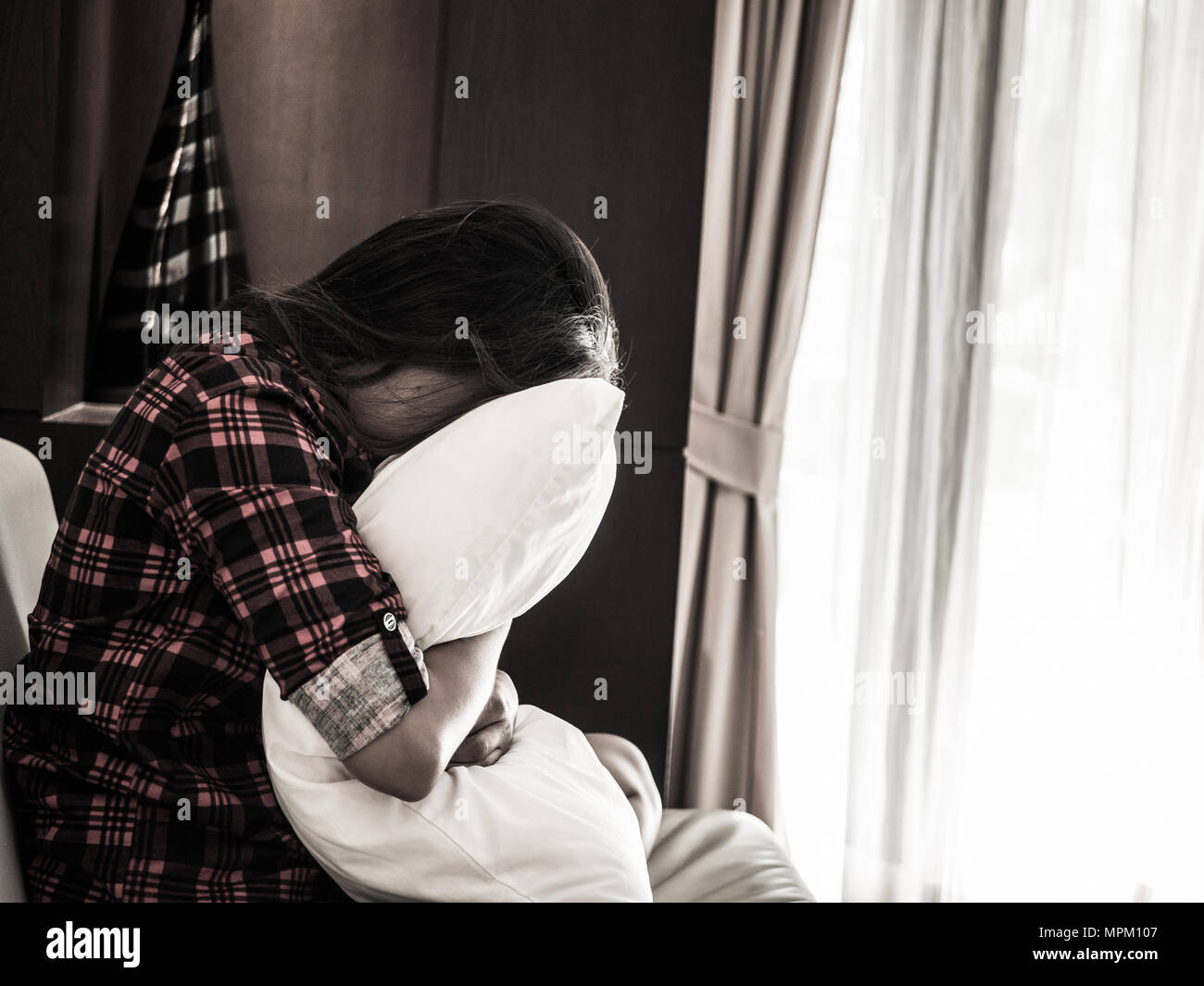 sad woman hug white pillow and cry. Sad woman sitting alone in a empty room beside window or door Stock Photo