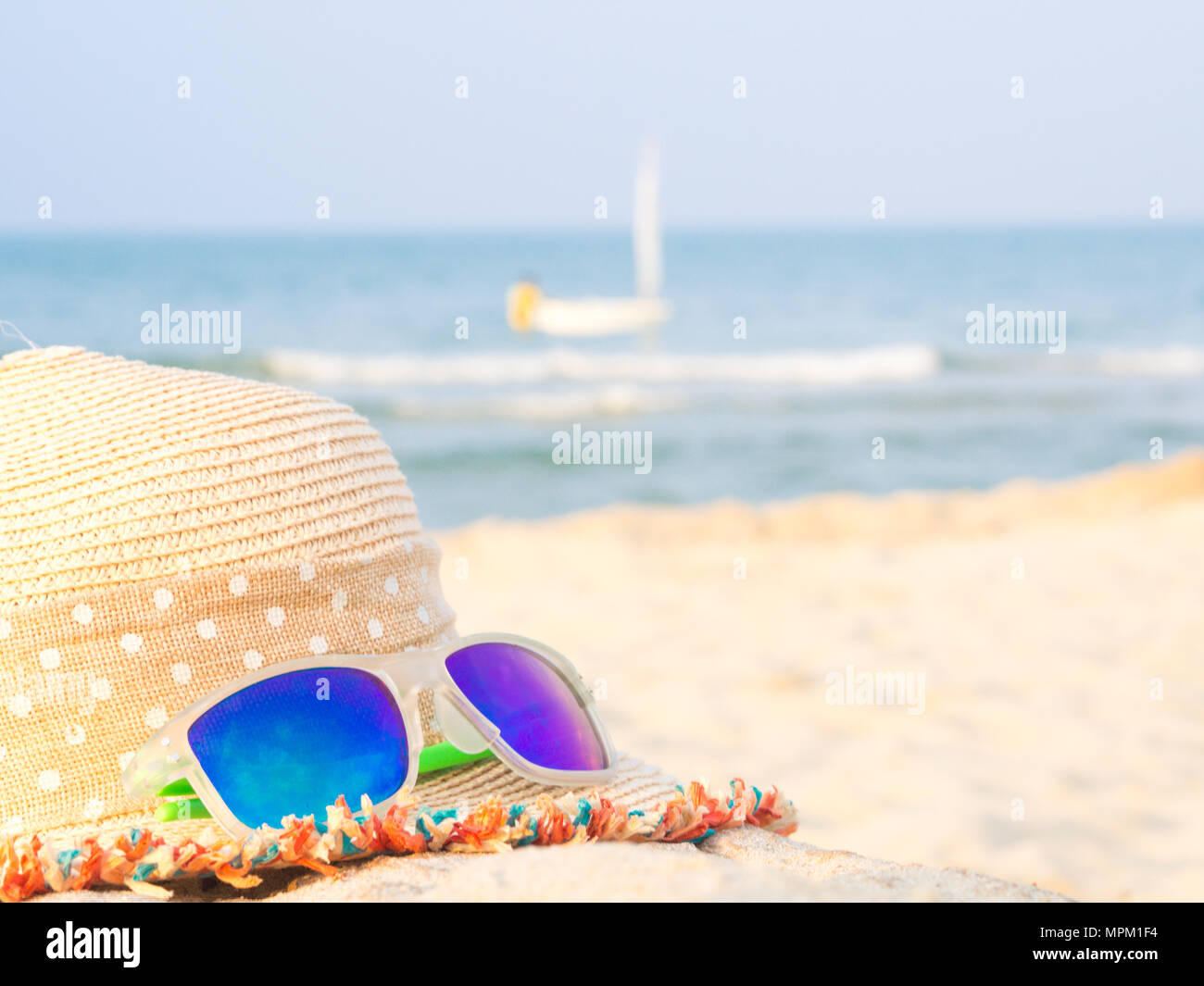 hat and sunglasses on the beach with sea and sailboat backround ...