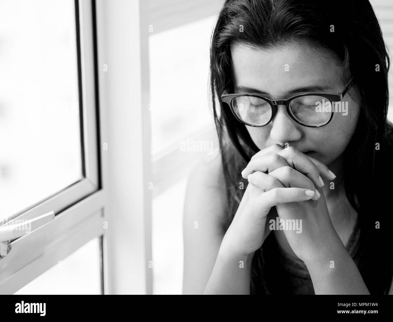 sad woman wear glasses sitting alone and praying near the window. Stock Photo
